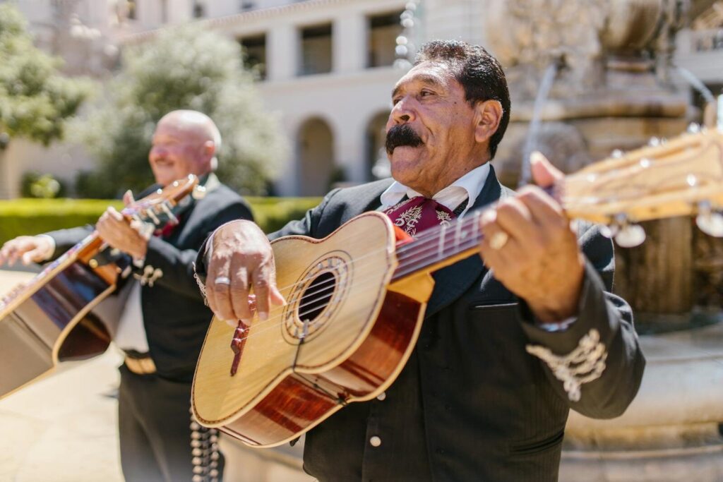 Two Mexican musicians play guitars joyfully in a festive outdoor setting.